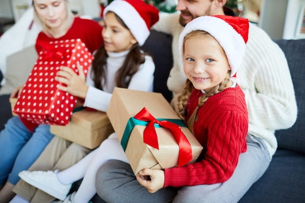 Famiglia felice che si siede sul divano e scartare i regali di Natale