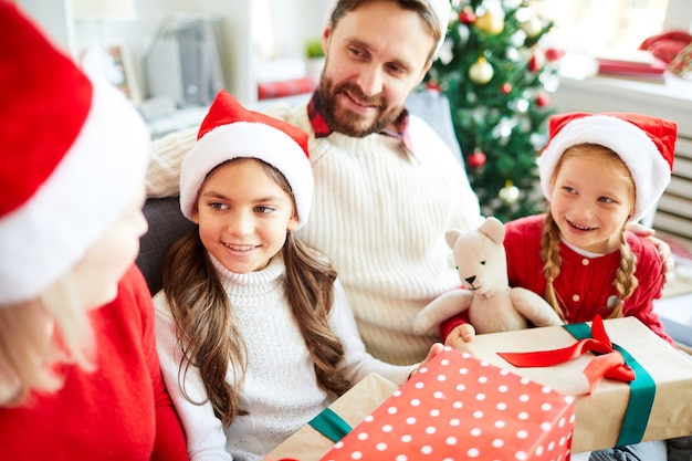 Famiglia felice che si siede sul divano e scartare i regali di Natale