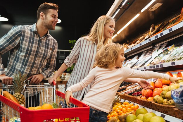 Famiglia felice con cibo d'acquisto del carrello e del bambino