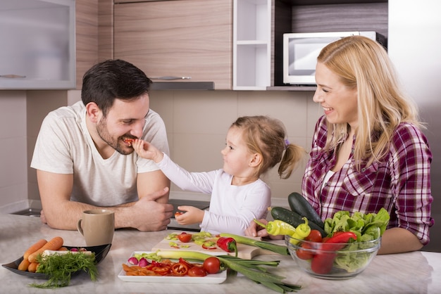 Famiglia felice con la loro piccola figlia che prepara un'insalata fresca con verdure in cucina