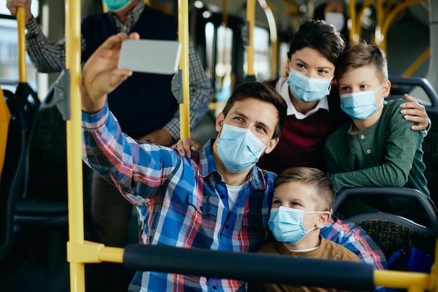 Famiglia felice con maschere facciali che si fanno selfie durante il pendolarismo in autobus