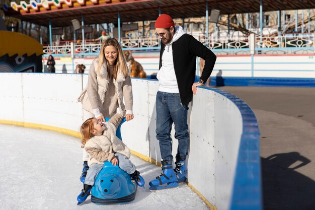 Famiglia felice del colpo pieno con il bambino alla pista di pattinaggio