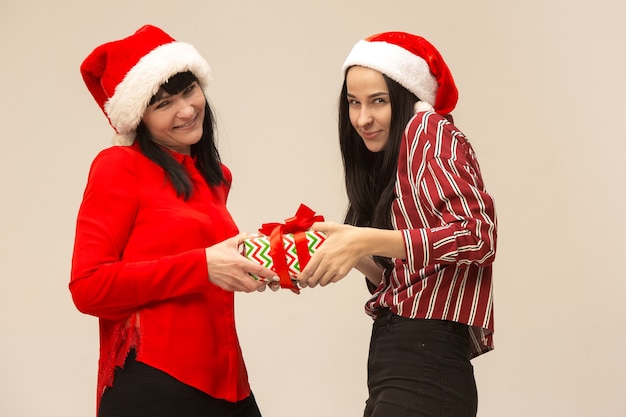 Famiglia felice in maglione di Natale in posa con i regali. Godersi gli abbracci d'amore, le persone in vacanza. Mamma e figlia su uno sfondo grigio in studio