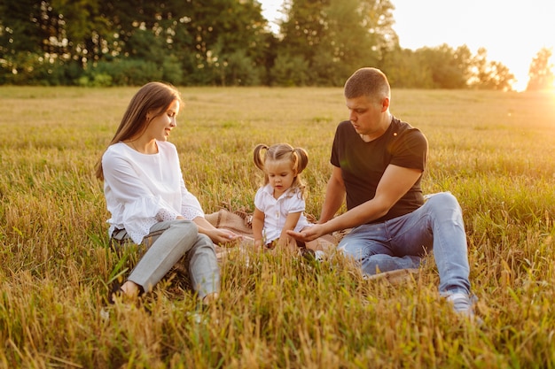 Famiglia felice in un campo in autunno. Madre, padre e bambino giocano nella natura sotto i raggi del tramonto