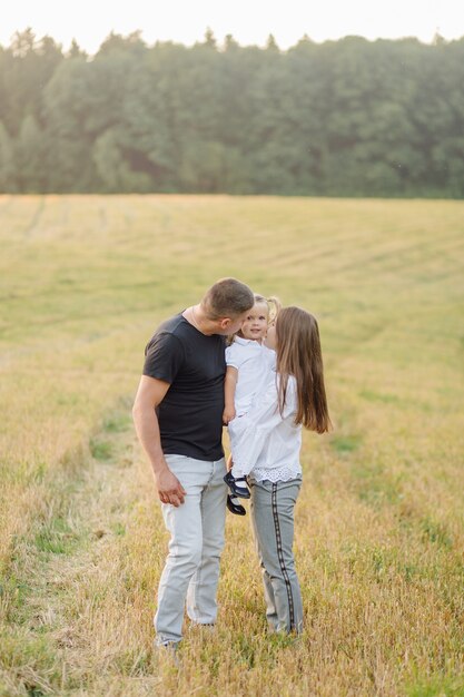 Famiglia felice in un campo in autunno. Madre, padre e bambino giocano nella natura sotto i raggi del tramonto