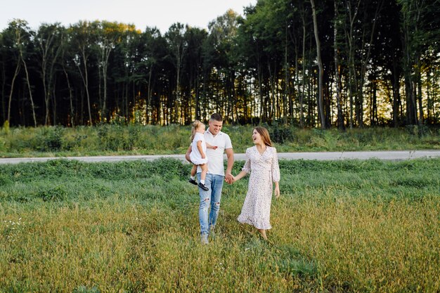 Famiglia felice in un parco in estate autunno. Madre, padre e bambino giocano nella natura sotto i raggi del tramonto