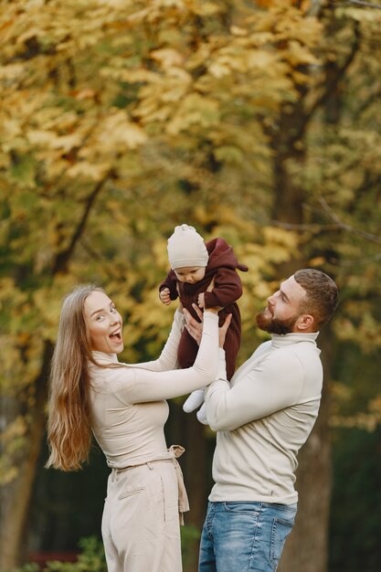 Famiglia in un parco d'autunno. Uomo con un maglione marrone. Bambina sveglia con i genitori.