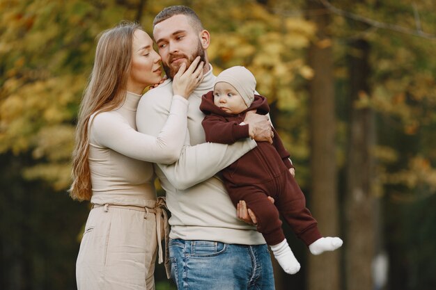 Famiglia in un parco d'autunno. Uomo con un maglione marrone. Bambina sveglia con i genitori.