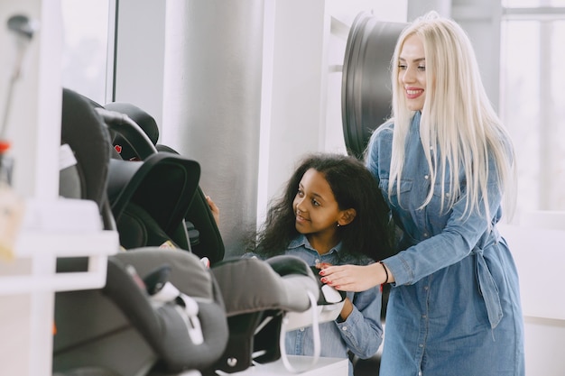 Famiglia in un salone di automobile. Donna che acquista il sedile dell'auto. Bambina africana con mther.