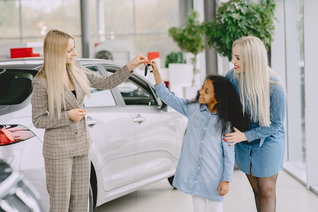 Famiglia in un salone di automobile. Donna che compra l'auto. Bambina africana con mther. Manager con i clienti.