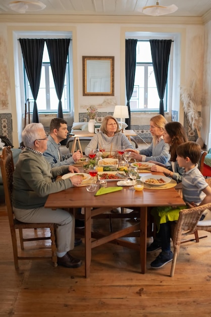 Famiglia multigenerazionale che cena insieme a casa. Coppia sposata seduta a tavola con figli e nonni e parlando. Concetto di festa in famiglia