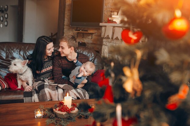 Famiglia seduta sul divano con albero di Natale fuori fuoco in fronte