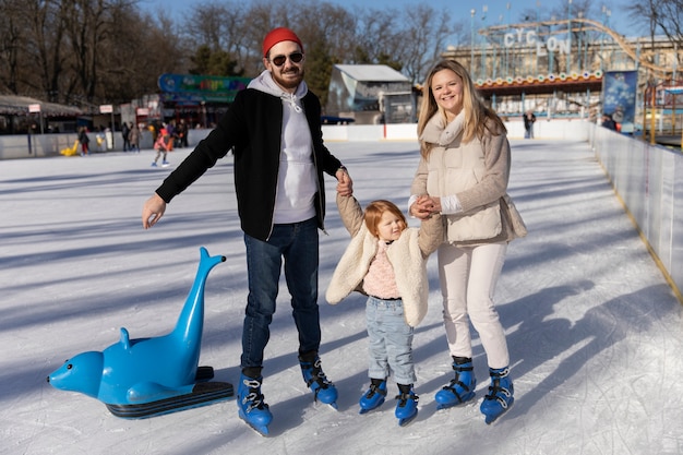 Famiglia sorridente del colpo pieno con il bambino alla pista di pattinaggio