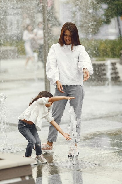 Famiglia vicino alla fontana della città. Madre con la figlia che gioca con l'acqua.