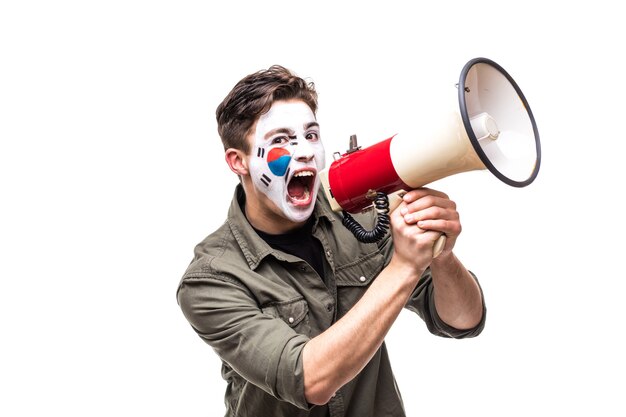 Fan fedele sostenitore bello dell'uomo della squadra nazionale della Repubblica di Corea con la faccia dipinta della bandiera che grida nel megafono con la mano appuntita. Fans le emozioni.