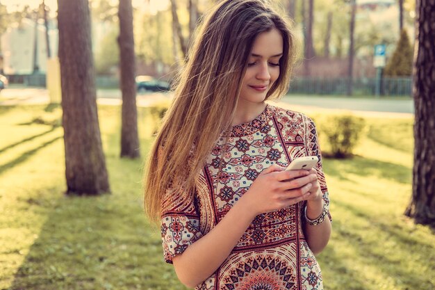 Fantastica giovane donna con smartphone in un parco selvaggio estivo.