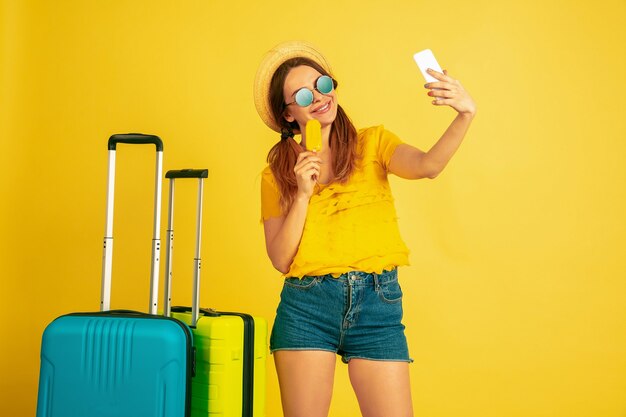 Fare selfie prima di partire. Ritratto della donna caucasica su sfondo giallo studio. Bellissimo modello in berretto. Concetto di emozioni umane, espressione facciale, vendite, annuncio. Estate, viaggi, resort.