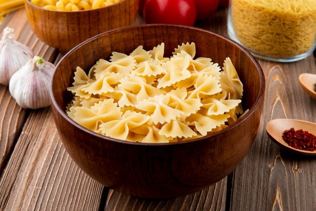 Farfale della pasta nella vista laterale dell'aglio di legno del pomodoro della ciotola