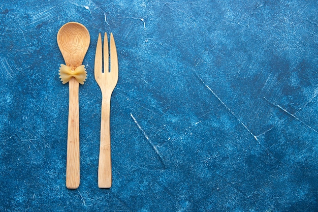 Farfalle del cucchiaio della forchetta di legno di vista superiore sul cucchiaio sulla tavola blu con spazio libero