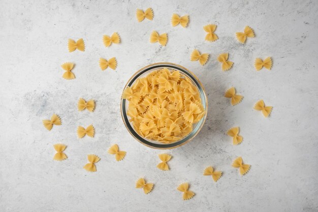 Farfalle di pasta in una ciotola di vetro su sfondo bianco.