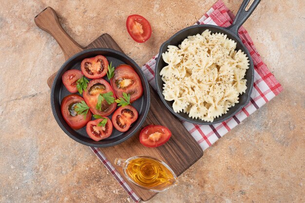 Farfalle e fette di pomodoro in padella nera con olio.