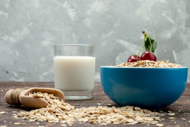 Farina d'avena cruda di vista frontale dentro il piatto blu su marrone, con la prima colazione cruda di salute degli alimenti a base di latte