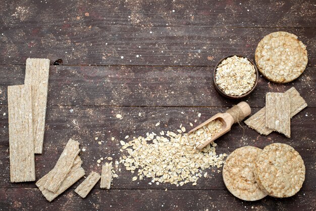 Farina d'avena cruda di vista superiore di colore chiaro con patatine fritte e cracker su marrone, colazione di salute utile pasto secco spuntino pane cracker