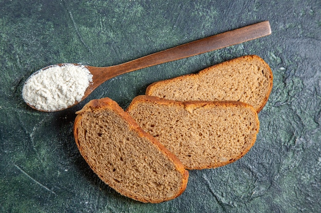 Farina vista dall'alto sul cucchiaio di legno con pagnotte di pane scuro sulla scrivania scura