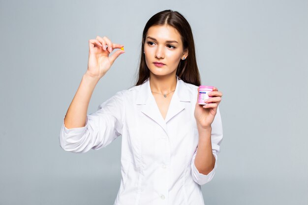 Farmaco femminile sorridente delle pillole della tenuta di medico isolato su una parete bianca.