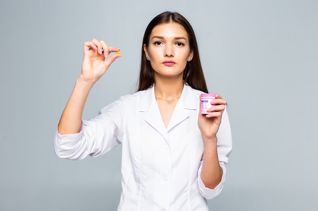 Farmaco femminile sorridente delle pillole della tenuta di medico isolato su una parete bianca.