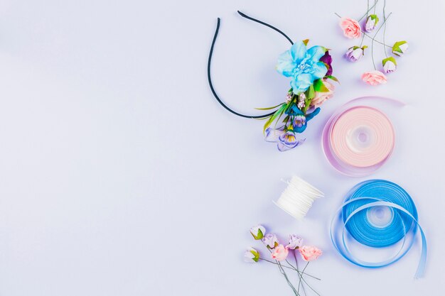 Fascia per capelli realizzata a mano con fiori artificiali; rocchetto e nastro su sfondo bianco