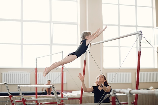 Fascio di equilibrio di ginnastica del bambino. Atleta ginnasta ragazza durante una barra orizzontale di esercizio nelle competizioni di ginnastica. Allenatore con bambino.