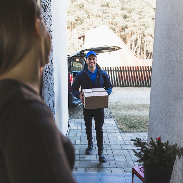 Fattorino allegro che porta scatola al cliente