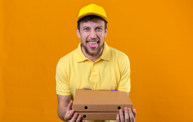 fattorino in maglietta polo gialla e berretto con scatole per pizza divertendosi con la lingua fuori in piedi sull'arancia