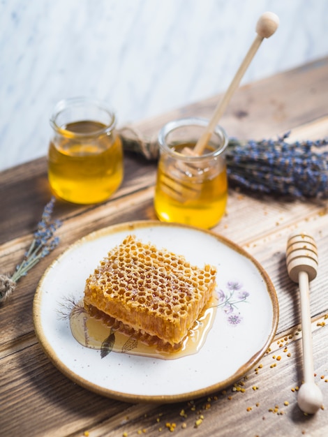 Favo a nido d&#39;ape sul piatto bianco con vaso di miele e lavanda sul tavolo di legno