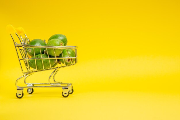 Feijoa verde fresco di vista frontale all'interno di un piccolo cesto in movimento su una superficie gialla di colore fruttato esotico