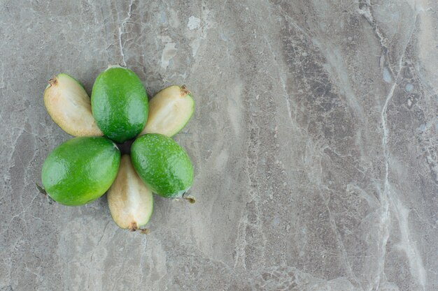 Feijoas interi e affettati disposti a motivo floreale su marmo.