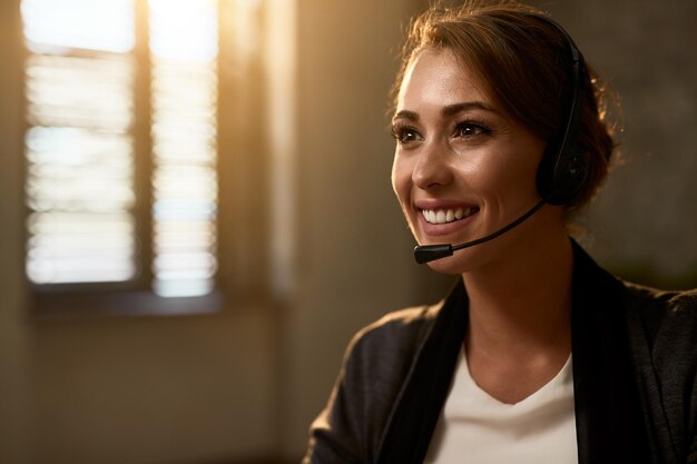 Felice agente del call center femminile che indossa la cuffia mentre lavora in ufficio