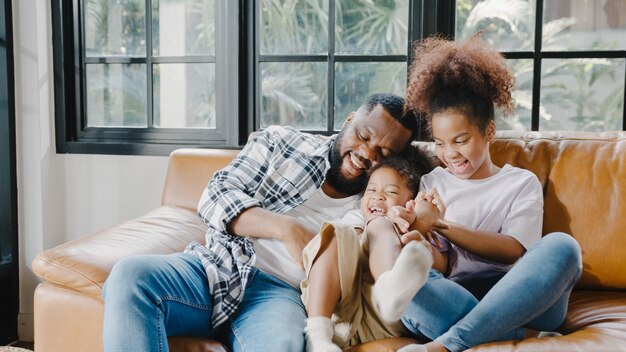 Felice allegra famiglia afroamericana papà e figlia che si divertono a coccolarsi sul divano durante il compleanno a casa.