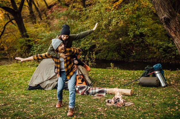 Felice amorevole coppia di turisti si diverte nella foresta vicino alla tenda e fa l'aeroplano