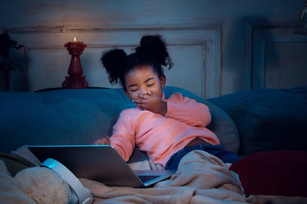 Felice bambina afroamericana durante la videochiamata con laptop e dispositivi domestici