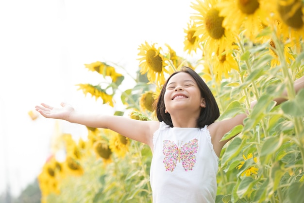 felice bambina asiatica divertendosi tra i girasoli fioriti sotto i dolci raggi del sole.