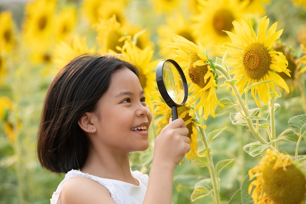 felice bambina asiatica divertendosi tra i girasoli fioriti sotto i dolci raggi del sole.