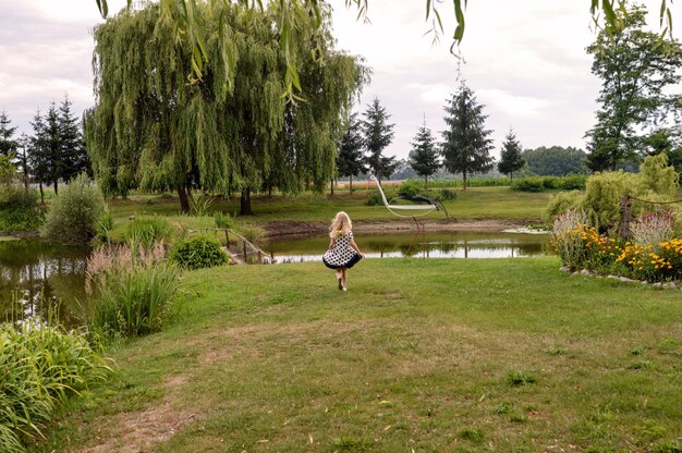Felice bambina in piedi davanti a uno stagno nel bellissimo giardino
