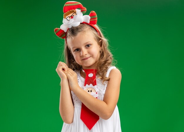 Felice bambina indossa il cerchio dei capelli di Natale con cravatta che tengono le mani insieme isolato su sfondo verde