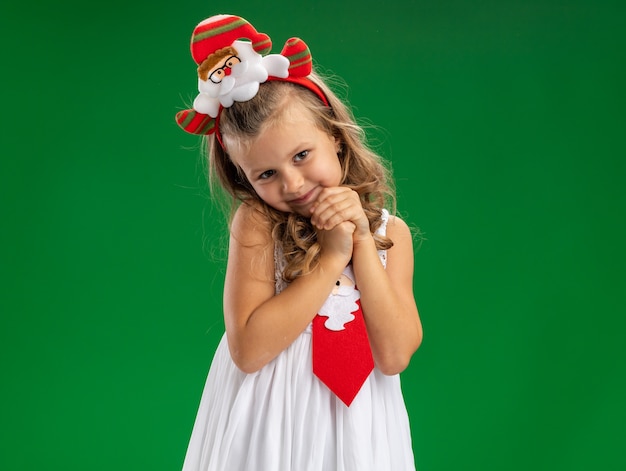 Felice bambina indossa il cerchio dei capelli di Natale con cravatta che tengono le mani insieme isolato su sfondo verde