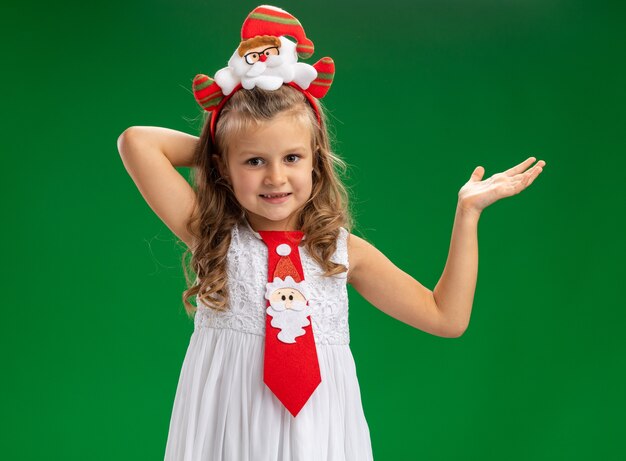 Felice bambina indossa il cerchio dei capelli di Natale con punti di cravatta con la mano a lato isolato su sfondo verde con spazio di copia