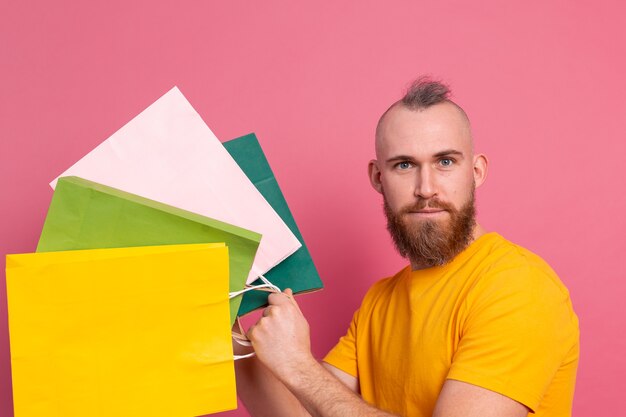 Felice barbuto uomo positivo look casual con borse della spesa colorate studio sfondo rosa