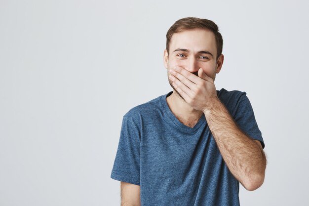 Felice bel ragazzo ridendo, coprire la bocca con il palmo