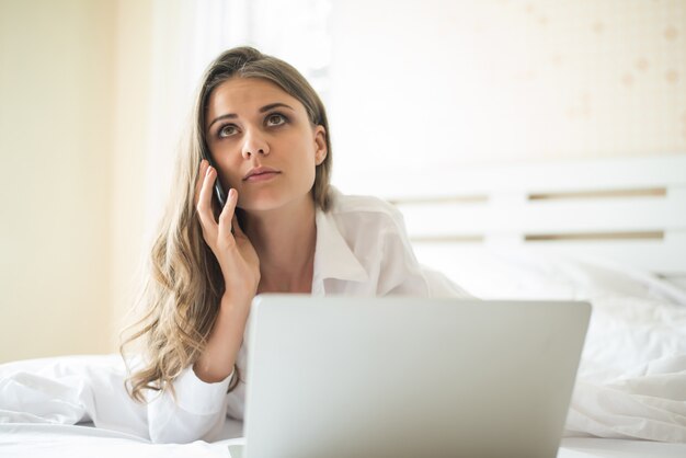 Felice bella donna che lavora su un computer portatile sul letto in casa